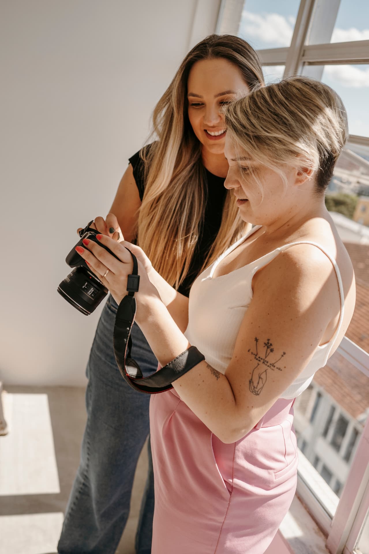 Lisi e uma mentorada olhando juntas a tela da câmera junto à janela